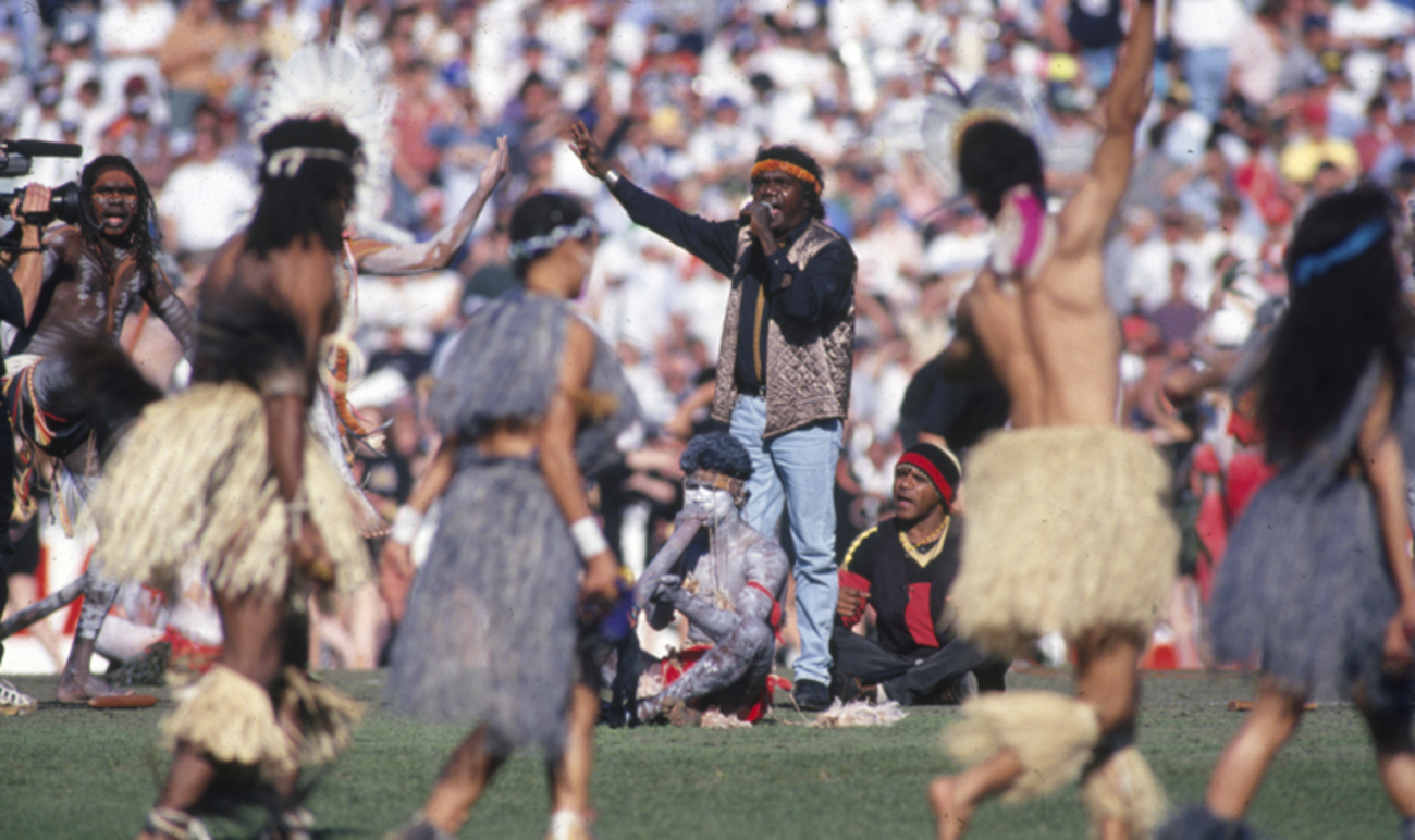 A man singing in front of a large crowd with dancers