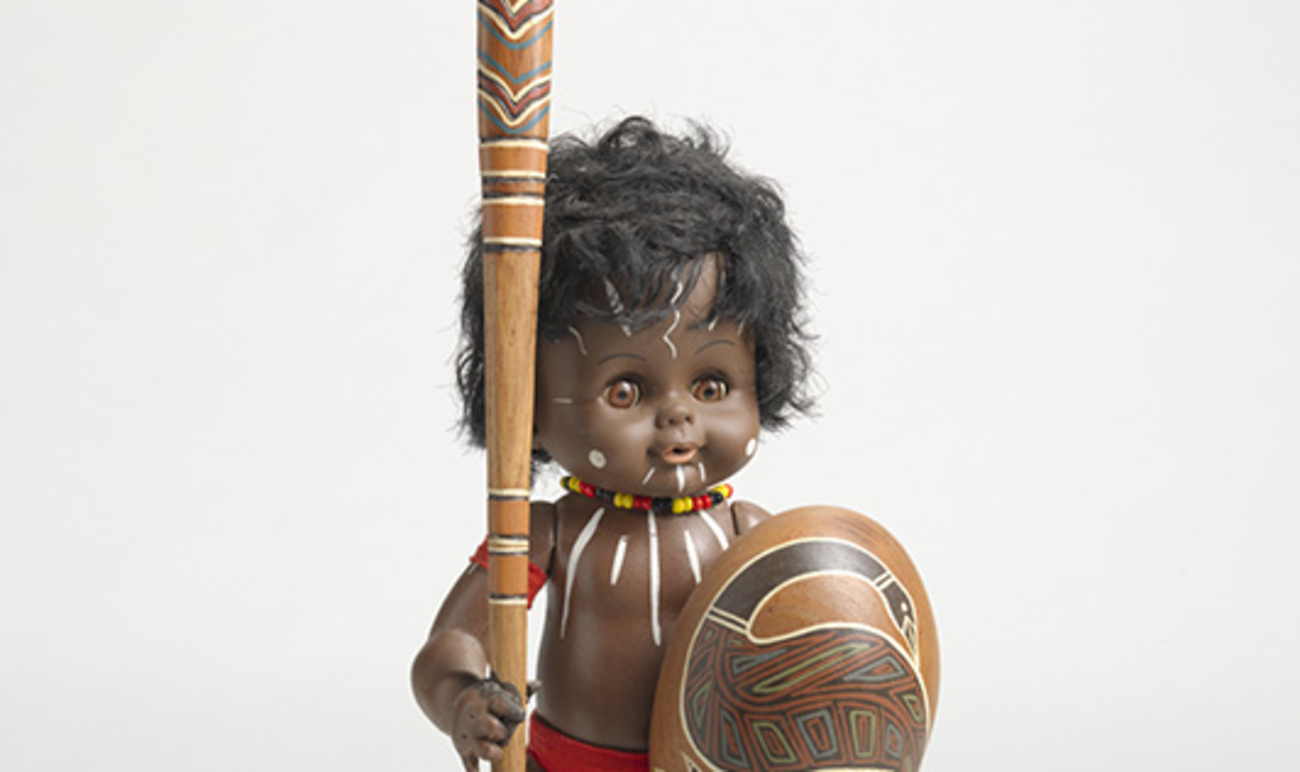 'Dolly' Plastic doll with acrylic paint and fabric mounted to wooden base with painted wooden shield, spear and boomerang. AIATSIS (AO R02181 - ATS 1078_063)