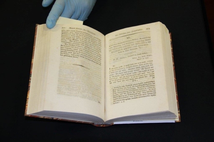 An open book with a gloved hand holding one of the pages