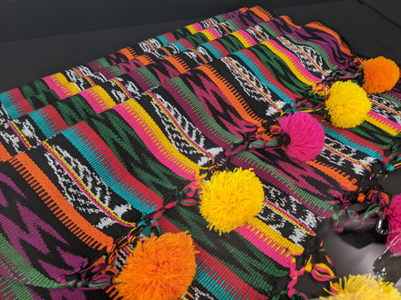 A colourful woven shawl with pom poms.